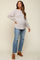 woman wearing a light gray oversized maternity sweater and distressed blue jeans, showing her baby bump