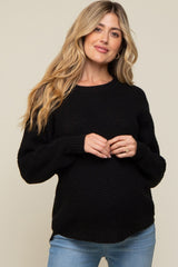 woman wearing a black maternity sweater with a textured knit pattern and a visible baby bump, paired with light blue jeans