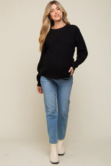 woman wearing a black maternity sweater and blue jeans, showing her baby bump while smiling at the camera