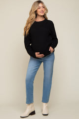 woman wearing a black knit maternity sweater and light blue jeans, holding her baby bump