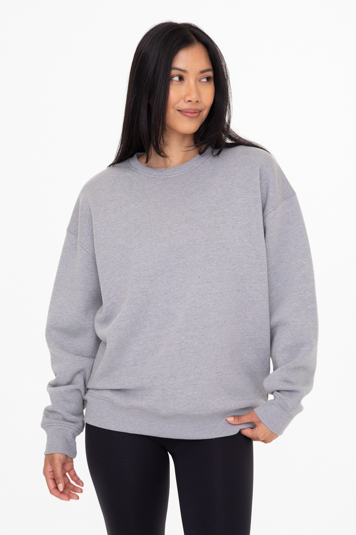 Woman wearing an oversized grey crewneck sweatshirt and black leggings against a white background