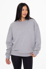 Woman wearing an oversized grey crewneck sweatshirt and black leggings against a white background