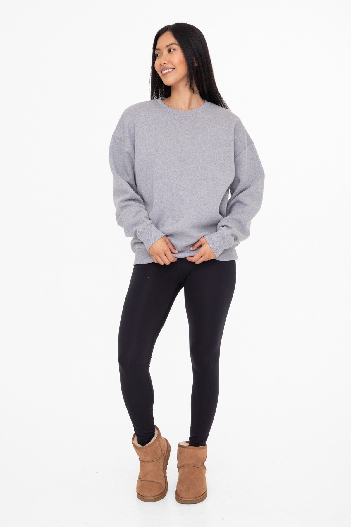 woman wearing a gray oversized sweatshirt, black leggings, and brown ankle boots, standing and smiling