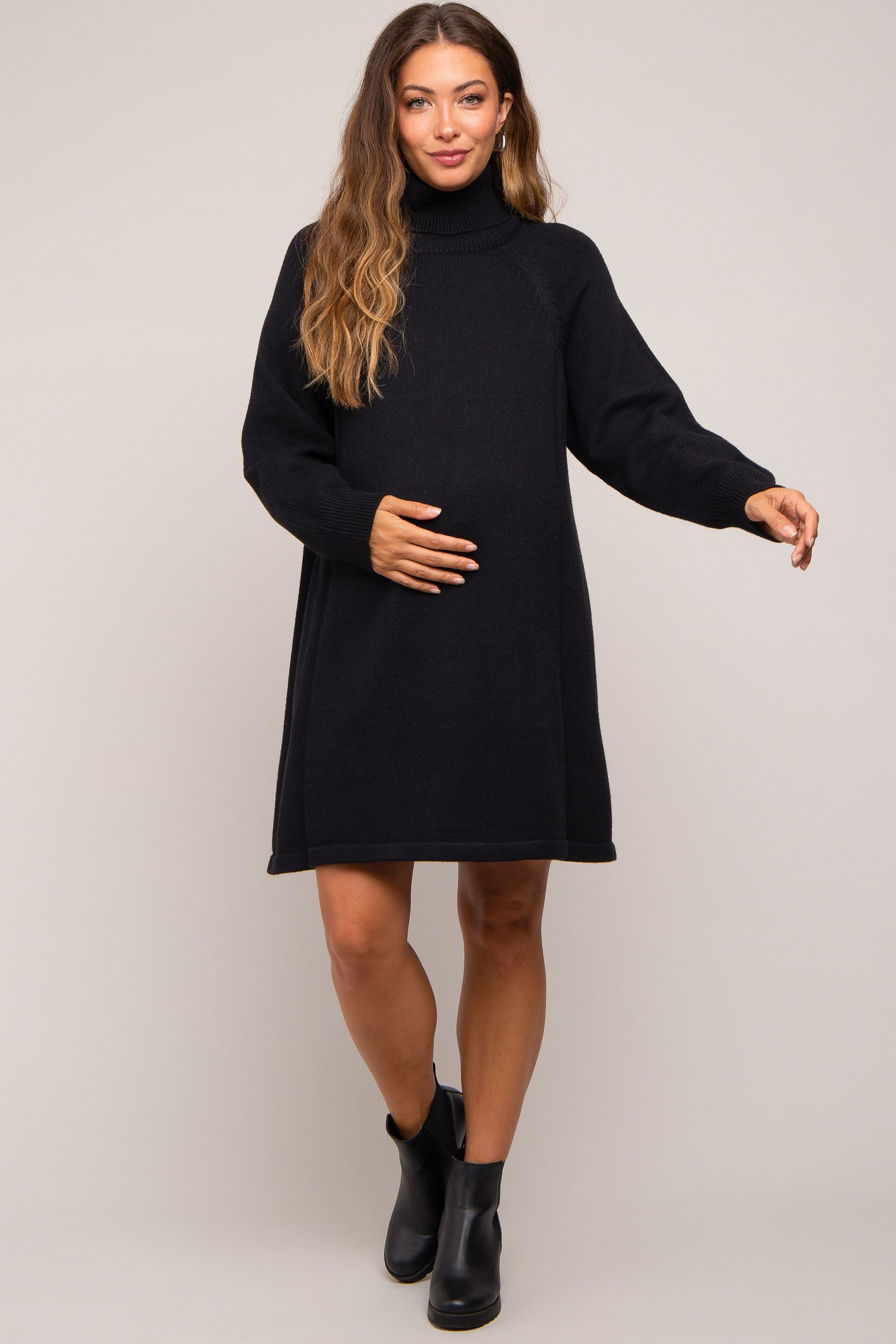 woman wearing a black knit maternity dress with a turtleneck and long sleeves, gently cradling her baby bump