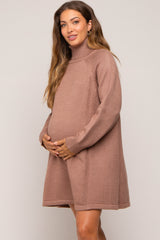 woman wearing a taupe maternity sweater dress with a turtleneck, gently cradling her baby bump