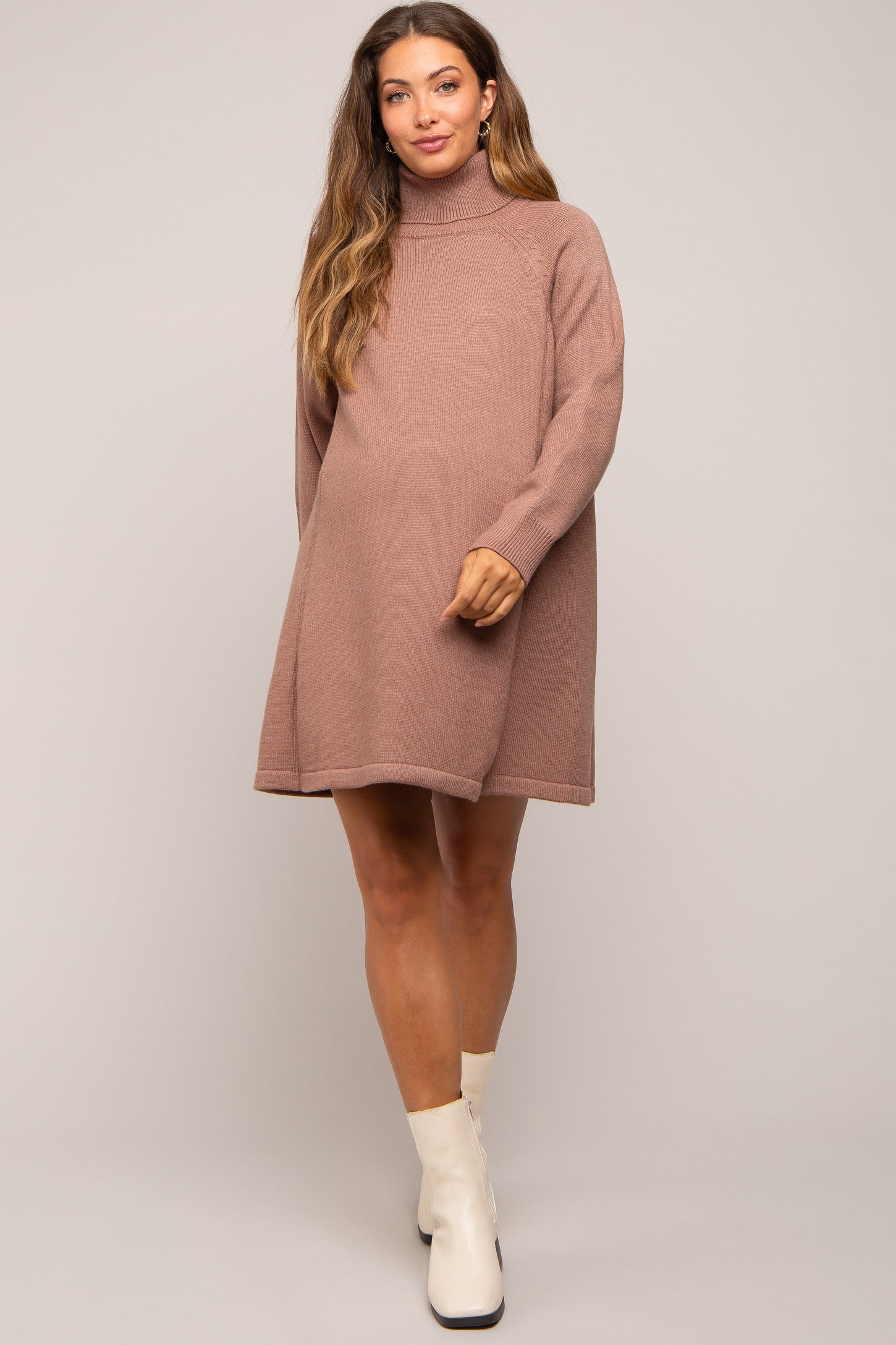 woman wearing a soft pink oversized maternity sweater dress with a turtleneck and a visible baby bump