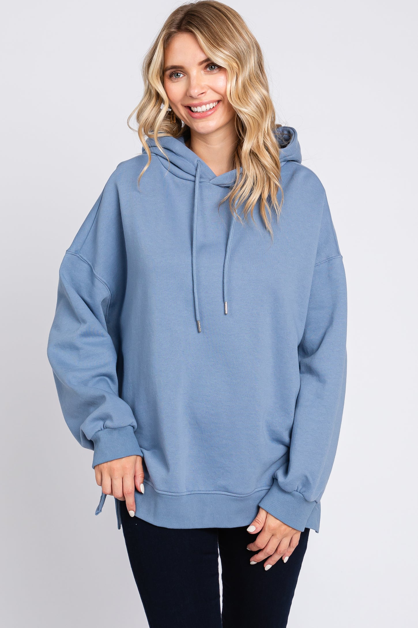 woman wearing a blue oversized hoodie with a drawstring and side slits, smiling at the camera
