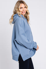 woman wearing a blue oversized hoodie with a side split and a drawstring hood, styled with dark jeans
