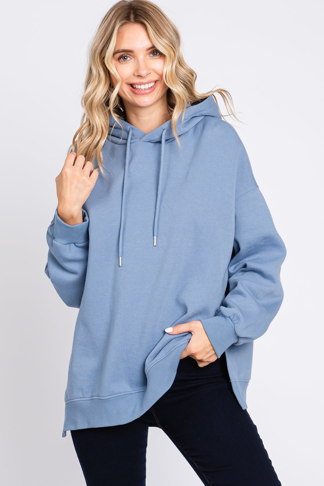 woman wearing a light blue oversized hoodie with a drawstring and side pockets, styled with dark jeans