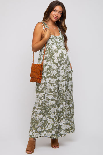 woman wearing a floral green maternity maxi dress with adjustable straps and holding a tan handbag