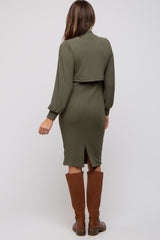 woman wearing an olive green ribbed midi dress with a cropped top and back slit, paired with knee-high brown boots
