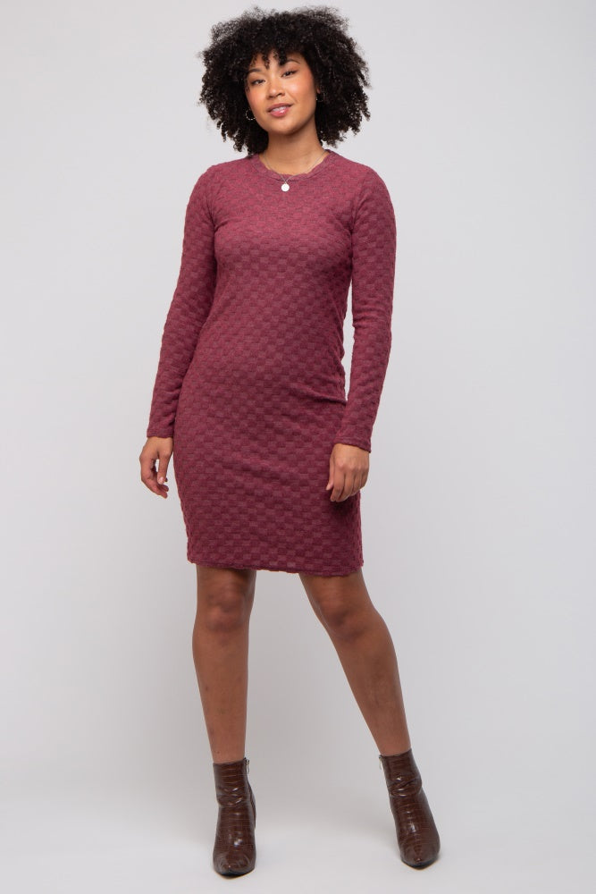 woman wearing a burgundy long sleeve textured dress with a round neckline and fitted style, standing confidently