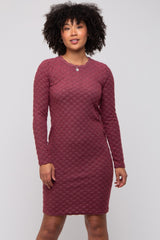 woman wearing a burgundy long sleeve fitted dress with a textured pattern and round neckline