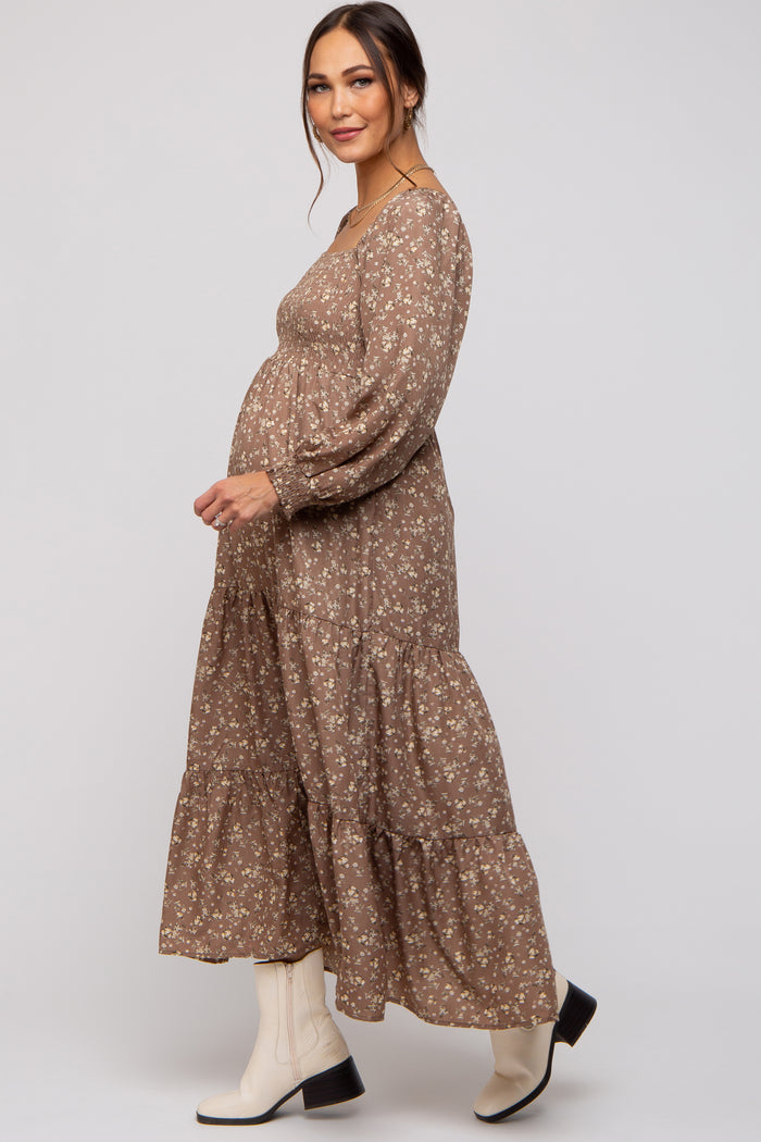 woman wearing a brown floral maternity maxi dress with a tiered skirt and long sleeves, showing her baby bump