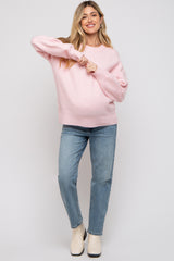 woman wearing a light pink maternity sweater and blue jeans, showing her baby bump while smiling