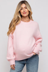woman wearing a light pink maternity sweater with a relaxed fit and long sleeves, showcasing her baby bump