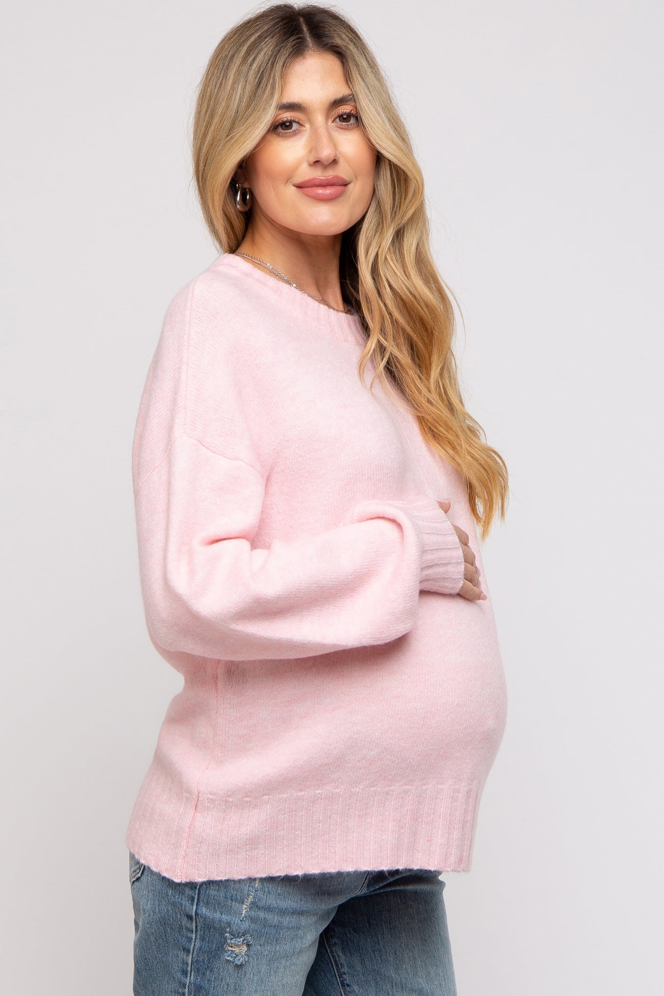 woman wearing a light pink oversized maternity sweater and holding her baby bump