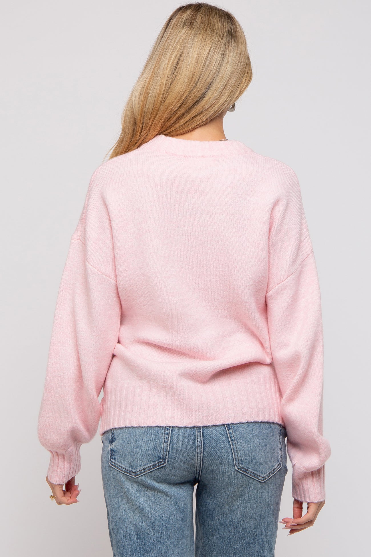 woman wearing a light pink oversized maternity sweater with a relaxed fit and ribbed hem, viewed from the back