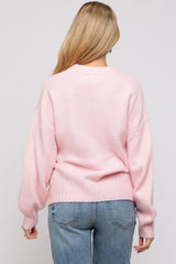 woman wearing a light pink oversized maternity sweater with a relaxed fit and ribbed hem, viewed from the back