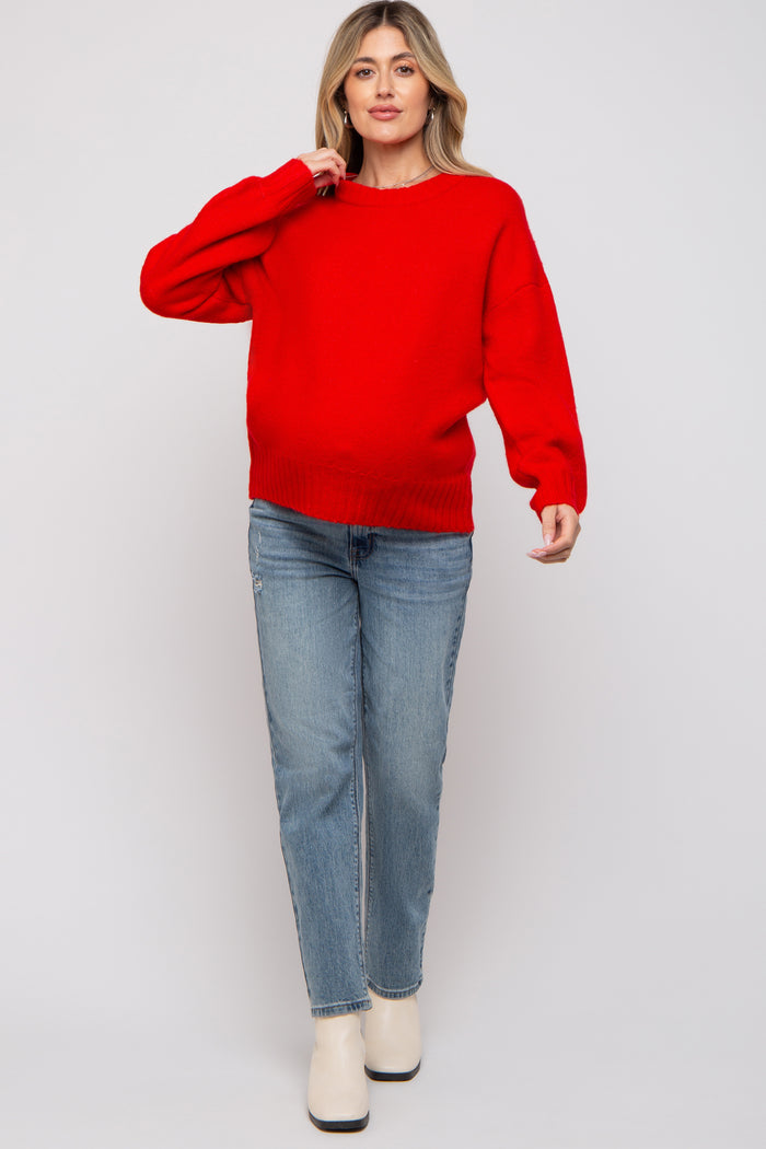 woman wearing a bright red maternity sweater and light blue jeans, showing a visible baby bump