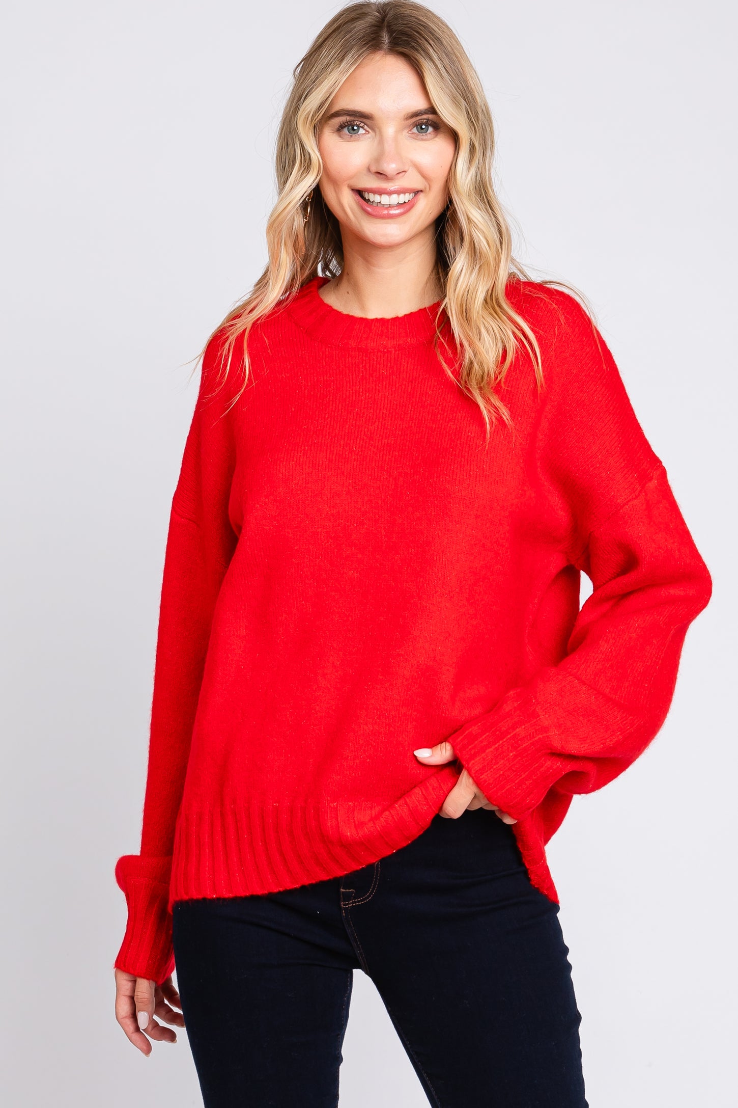 woman wearing a vibrant red oversized sweater with long sleeves and a ribbed hem, smiling at the camera