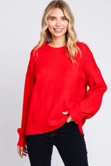 woman wearing a vibrant red oversized sweater with long sleeves and a ribbed hem, smiling at the camera