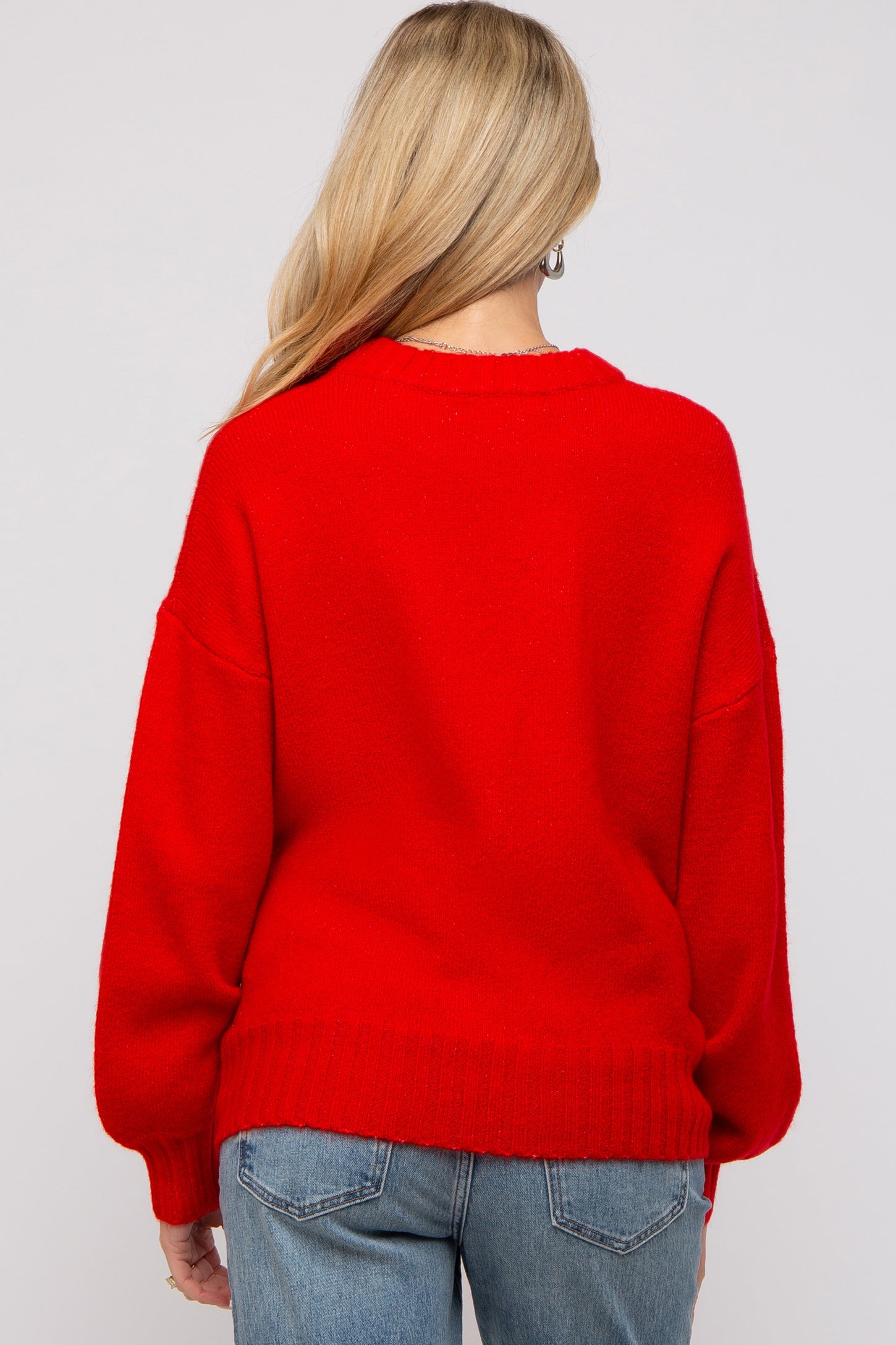 woman wearing a bright red oversized maternity sweater with a relaxed fit, styled with denim jeans