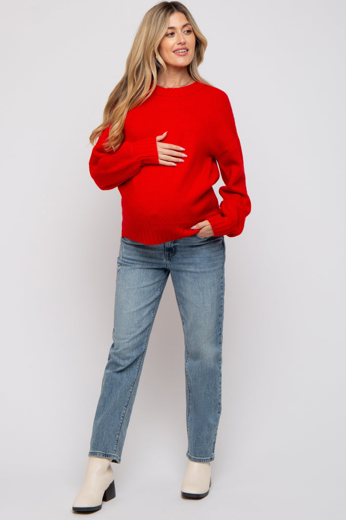 woman wearing a red maternity sweater and blue jeans while holding her baby bump