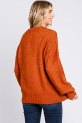 woman wearing an oversized orange knit sweater, showing the back view, paired with dark blue jeans