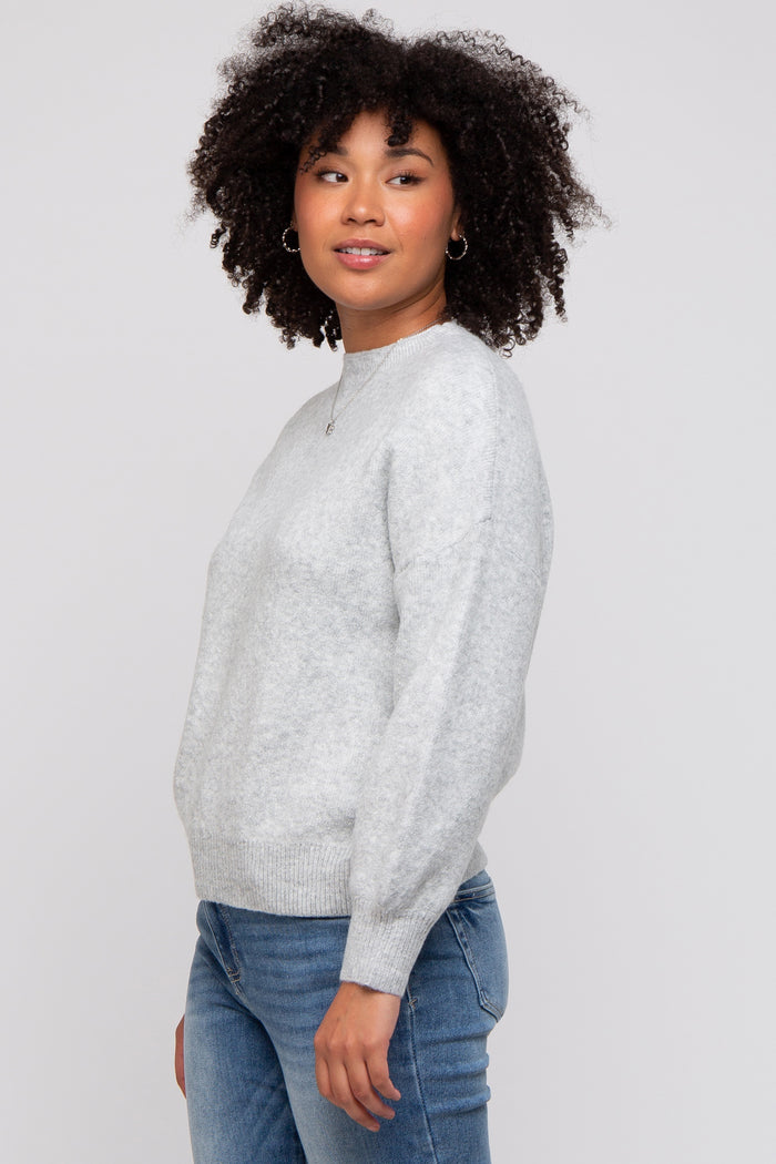 woman wearing a light gray sweater with a round neckline and long sleeves, paired with blue jeans