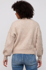 woman wearing a beige oversized sweater with balloon sleeves, seen from the back, paired with light blue jeans