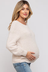woman wearing a soft beige maternity sweater and cradling her baby bump, paired with light blue jeans