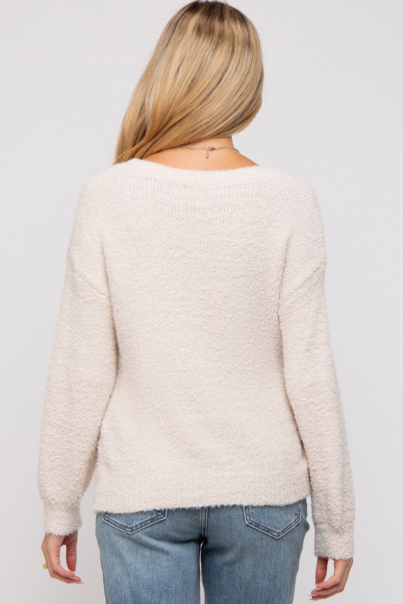 woman wearing a light beige maternity sweater with a soft texture, viewed from the back, paired with blue jeans