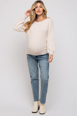 woman wearing a light beige maternity sweater with long sleeves and blue maternity jeans, showing her baby bump