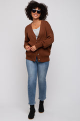 woman wearing a brown oversized cardigan with buttons, gray top, blue jeans, and black ankle boots, smiling and wearing sunglasses
