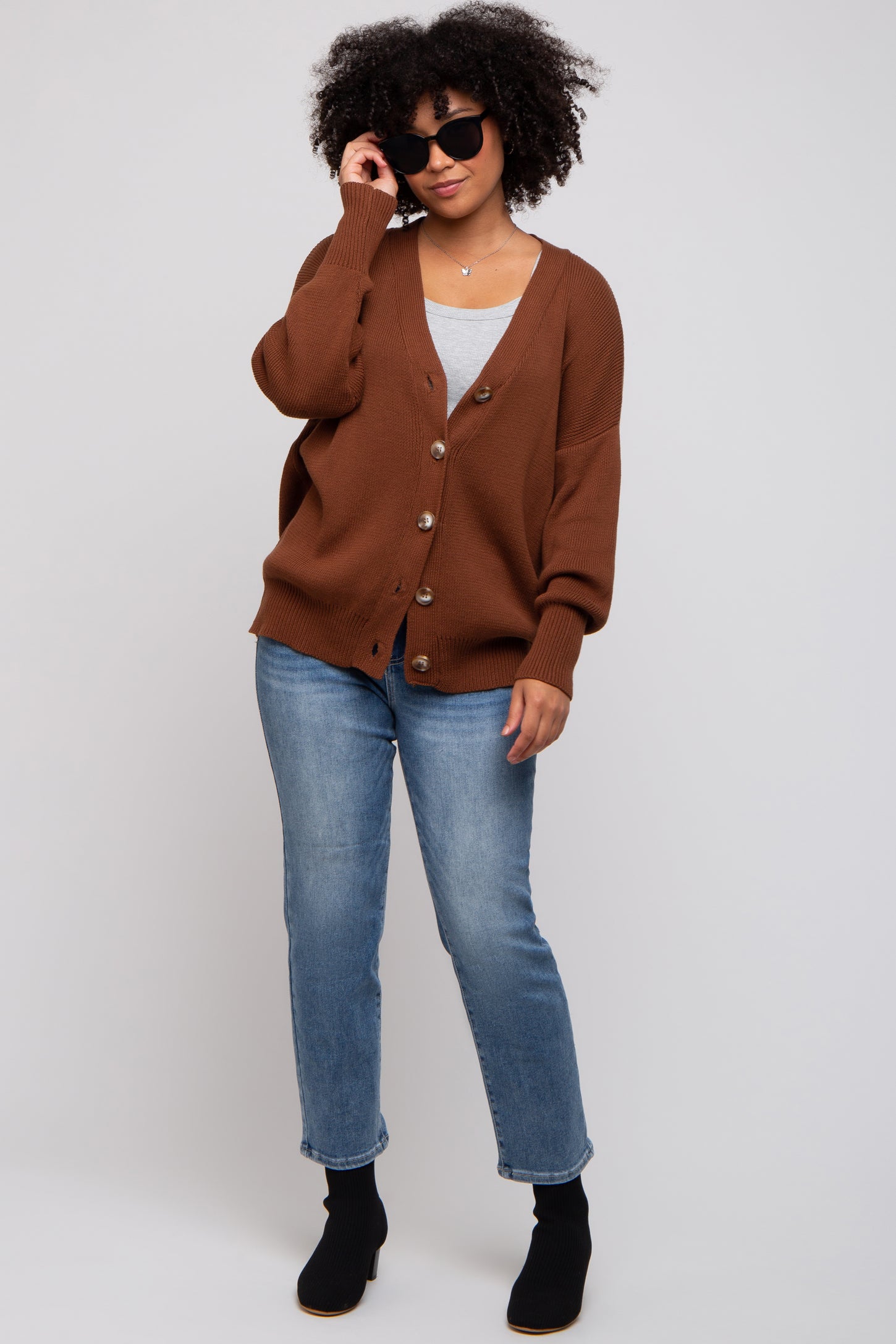 woman wearing a brown oversized cardigan with buttons, styled with a light gray top and blue jeans, accessorized with sunglasses