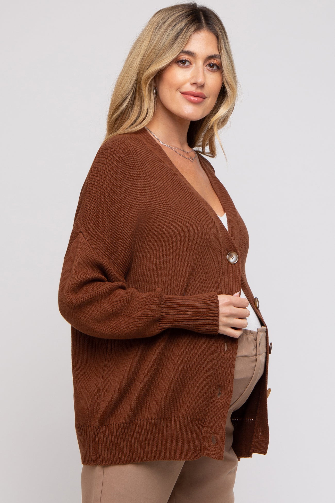 woman wearing a rust brown button-up maternity cardigan over a white top and showcasing her baby bump