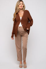 woman wearing a brown oversized cardigan with buttons and beige maternity pants, styled with a white top