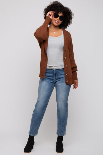 woman wearing a brown button-up cardigan over a grey tank top and blue jeans, accessorized with black sunglasses and ankle boots