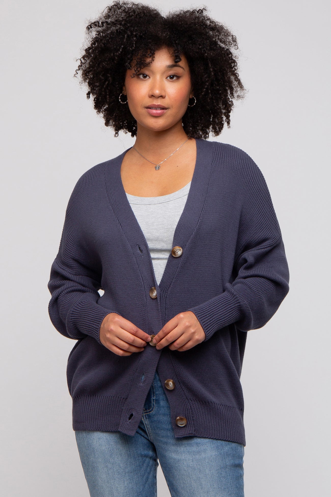woman wearing a navy blue oversized cardigan with button details and a gray top underneath, standing against a light background