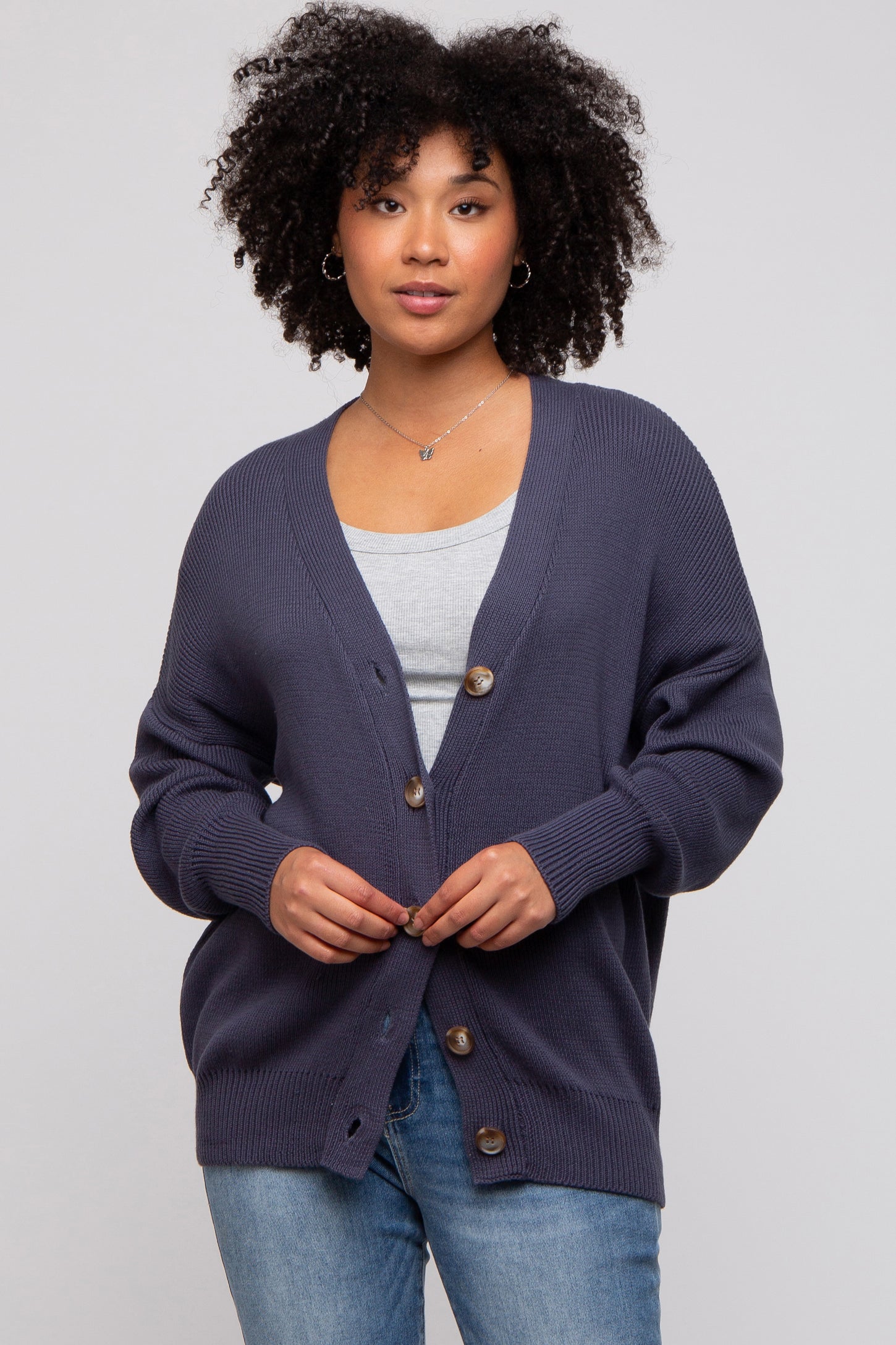 woman wearing a navy blue oversized cardigan with button details and a gray top underneath, standing against a light background