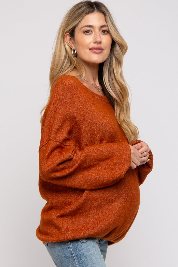 woman wearing an orange oversized maternity sweater and showing her baby bump