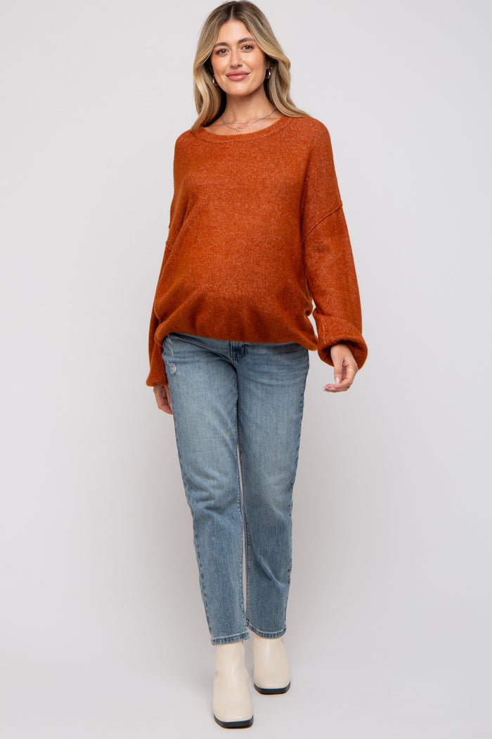 woman wearing an oversized rust orange maternity sweater and light blue jeans, showing her baby bump
