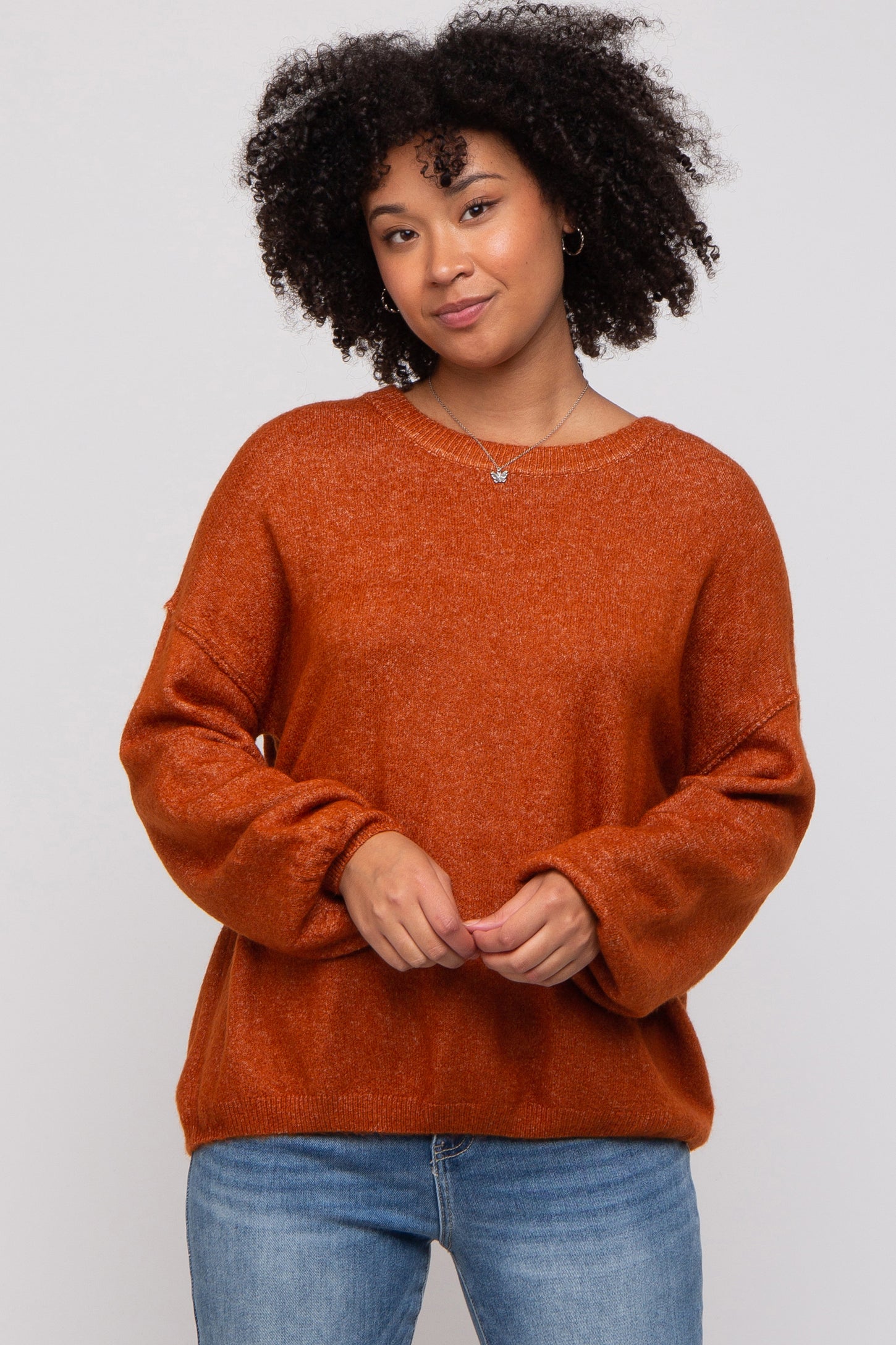 woman wearing an oversized burnt orange sweater with long sleeves and a round neckline, paired with light blue jeans