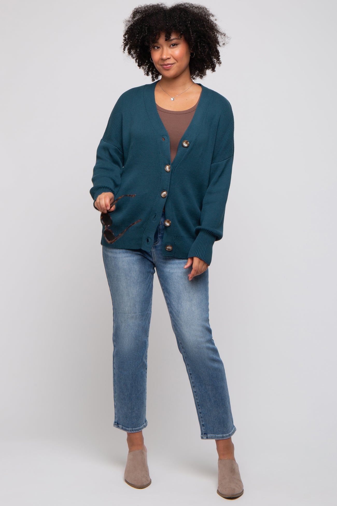 woman wearing a teal oversized cardigan with buttons, paired with a brown top and light blue jeans, styled with beige ankle boots