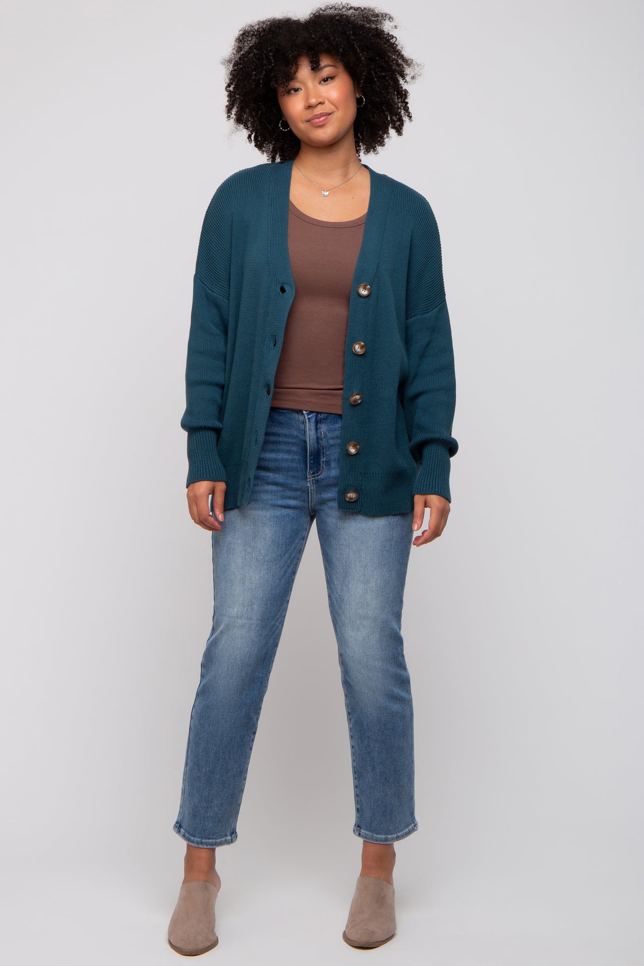 woman wearing a teal button-up cardigan over a brown top and light blue jeans with gray slip-on shoes