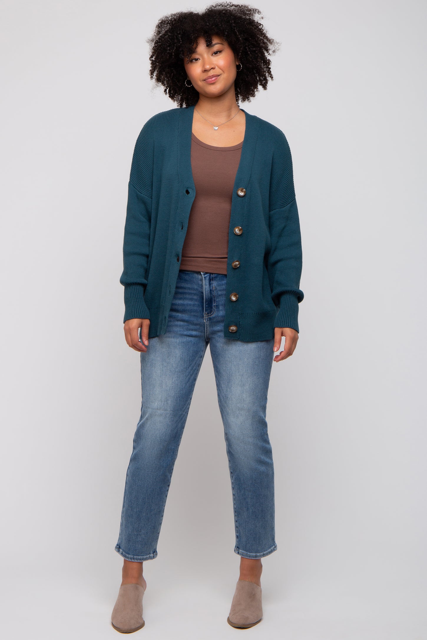 woman wearing a teal button-up cardigan over a brown top and light blue jeans with gray slip-on shoes