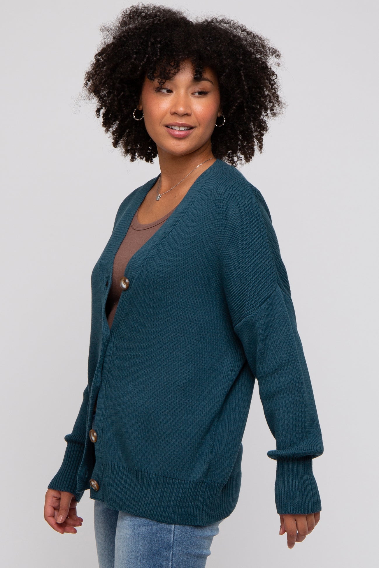 woman wearing a teal oversized cardigan with buttons and a v-neck, paired with a brown top and jeans