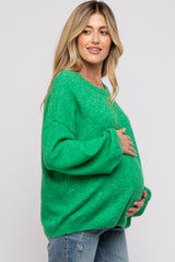 woman wearing a green oversized maternity sweater and cradling her baby bump