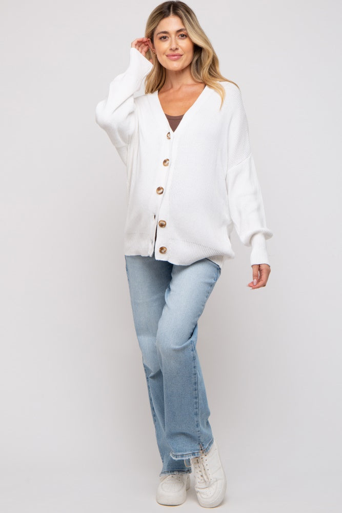 woman wearing a white button-up maternity cardigan over a black top and blue jeans, smiling at the camera